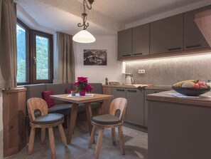 Eine moderne Küche mit Essbereich, Holzkohle-Stühle, einem Tisch, einer Pendelleuchte und Blick ins Grüne.
