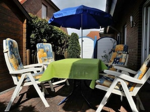 An outdoor seating area with a table covered by a green tablecloth and a blue umbrella. - Lower Apartment "dornum" (Dornum)