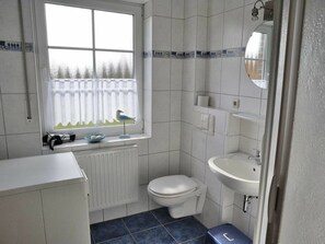 A bathroom with a toilet, sink, and window with a bird decoration. - Lower Apartment "dornum" (Dornum)