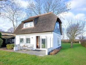 A house with a thatched roof, a large glass door, and a small patio with a table and chairs. - Holiday Home in Den Burg With Swimming Pool (Den Burg)