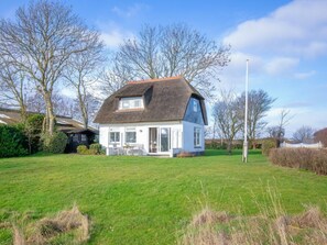 A white house with a thatched roof, a lawn, and trees in the background. - Holiday Home in Den Burg With Swimming Pool (Den Burg)