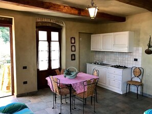 A kitchen with white cabinets, a gas stove, and a sink. There is a dining table with a pink tablecloth and two chairs. - Holiday Apartment With 2 Bedrooms (Massa Marittima)