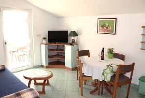 Ett kompakt vardagsrum med en soffa, ett matbord med stolar, en TV på ett TV-bord och en liten bokhylla.