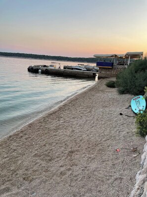 Ein Strand mit felsigem Ufer, einer Anlegestelle mit Booten und einem Gebäude mit überdachtem Bereich.