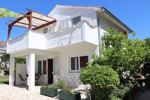 Ein zweistöckiges Haus mit überdachter Terrasse, Balkon und Garten.