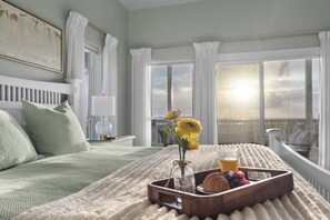 Ein ordentlich bezogenes Bett, ein Tablett mit Frühstücksangeboten, eine Vase mit Blumen und ein Blick auf den Himmel durch das Fenster.