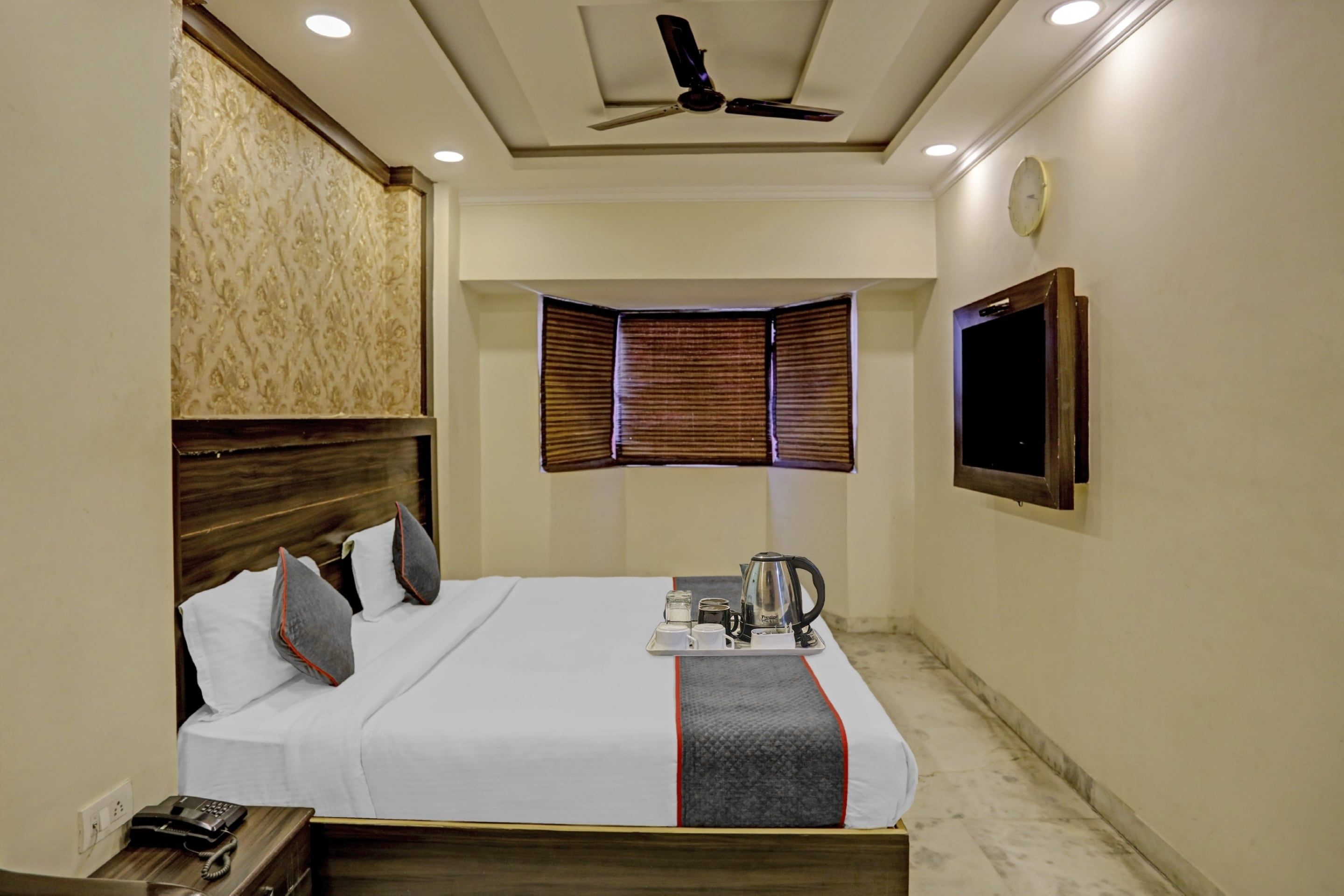 Une chambre d’hôtel équipée d’un lit, d’un téléphone sur la table de chevet, d’un plateau avec une bouilloire et des tasses, d’un ventilateur de plafond et d’un téléviseur fixé au mur.