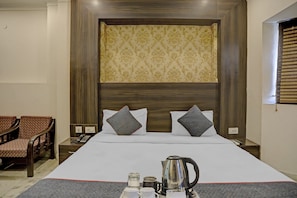 Habitación de hotel con una cama grande, dos almohadas, una mesita de noche con teléfono y una ventana con persianas.