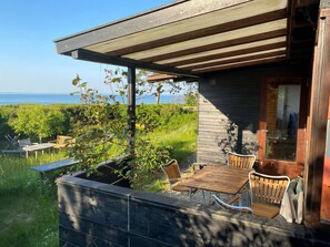 A wooden deck with a table and chairs, overlooking a grassy area and the sea. - 4 Star Holiday Home in Hornbaek (Hornbaek)