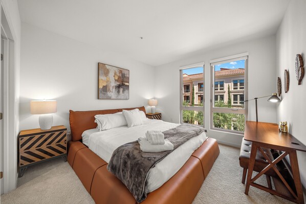 Une chambre d’hôtel avec un lit, des tables de chevet, un bureau et une fenêtre donnant sur des immeubles.