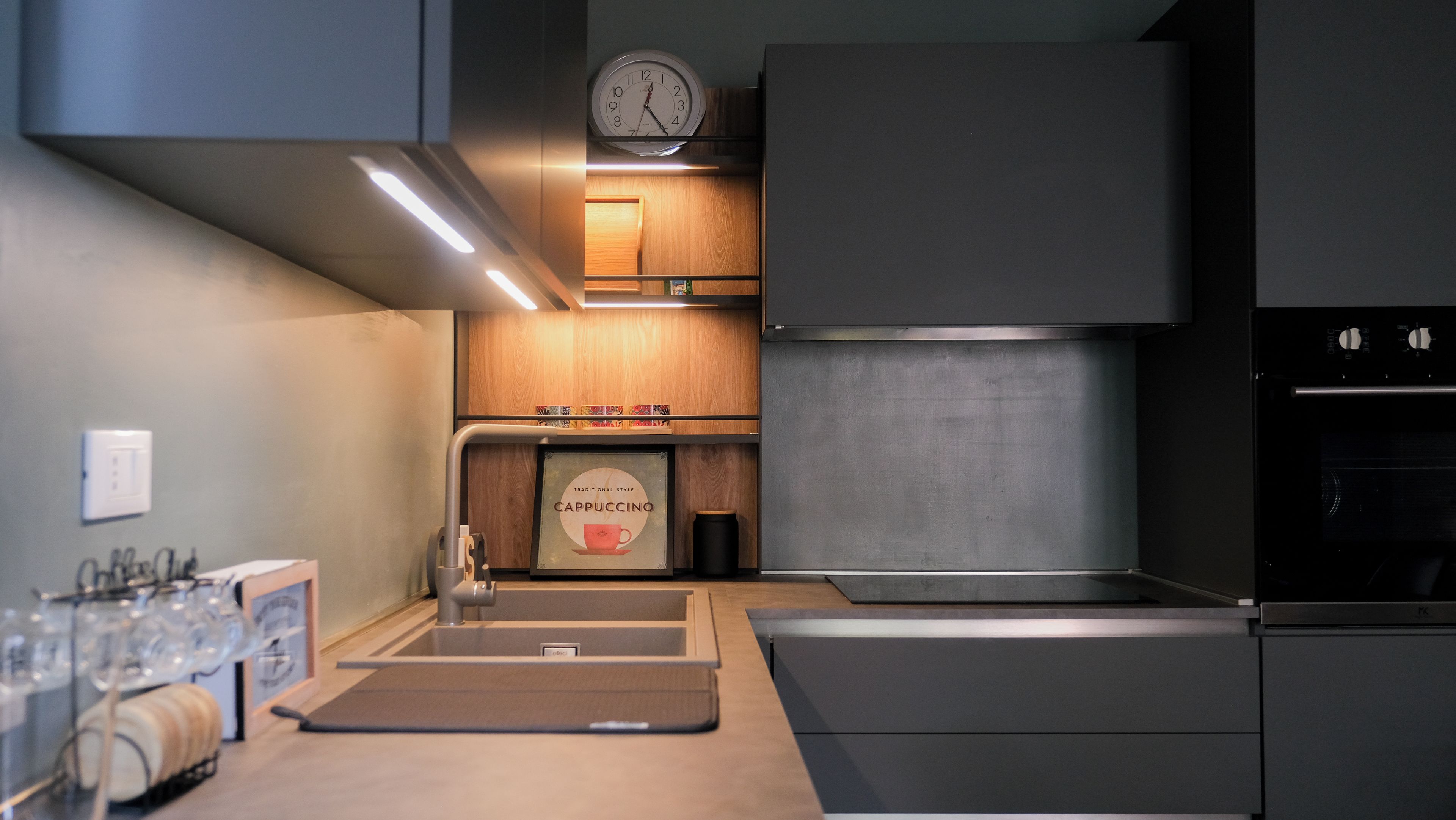 A modern kitchen with a built-in oven, a clock, and a coffee machine.