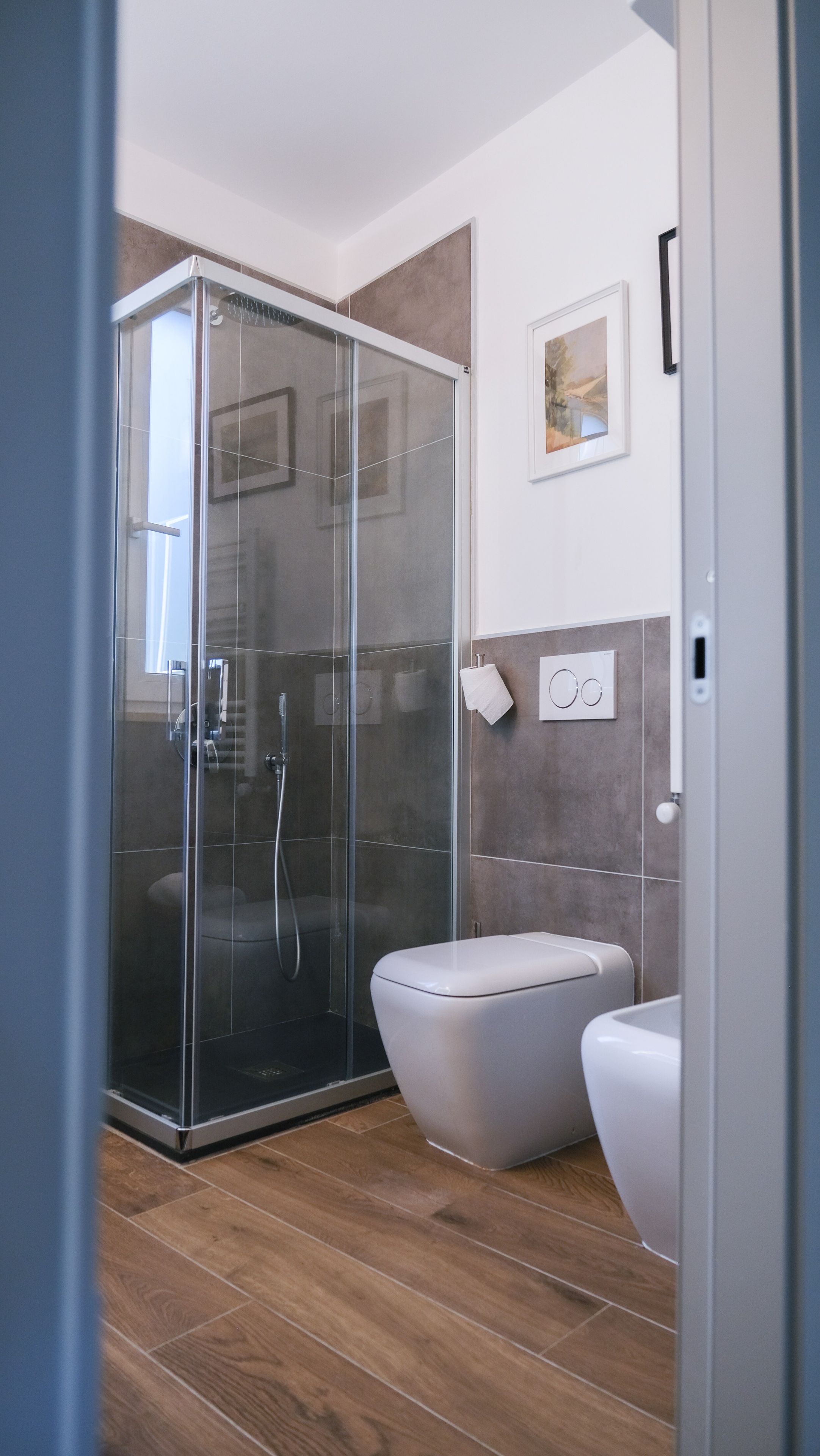 A modern bathroom with a glass-enclosed shower, a toilet, and a wall-mounted bidet.