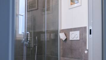 A modern bathroom with a glass-enclosed shower, a toilet, and a wall-mounted bidet.
