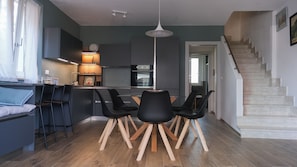 A modern kitchen with a central island, black chairs, and a wooden floor.