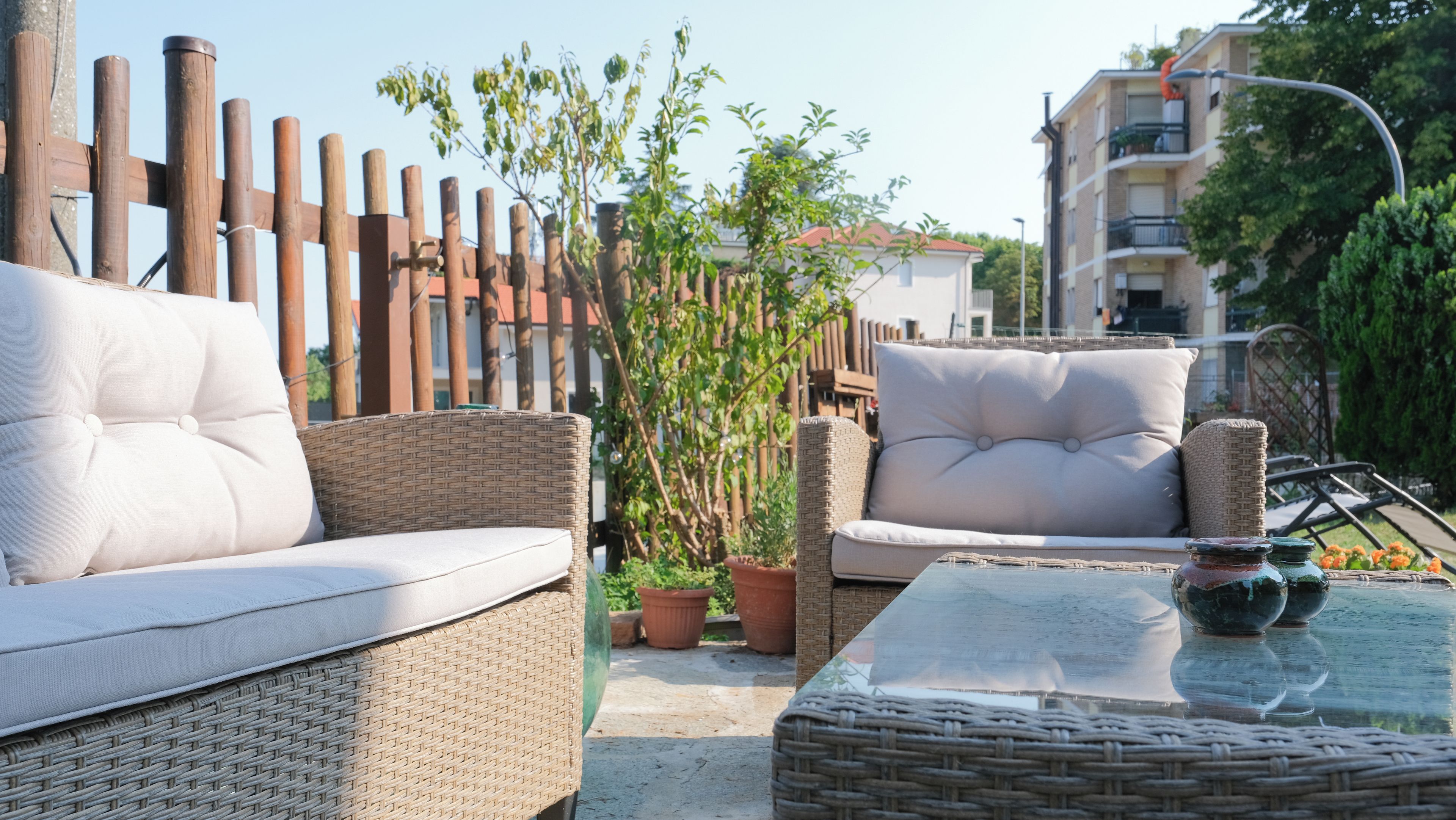 A patio area with wicker furniture, including two sofas and a table, surrounded by a wooden fence and potted plants.