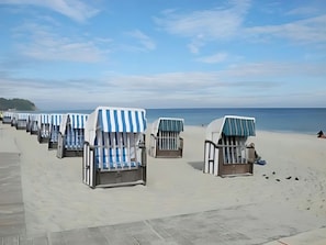 Eine Reihe von Liegestühlen am Strand, mit gestreifter Markise, feinem Sand und dem Meer im Hintergrund.