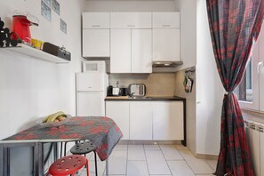 A compact kitchen with white cabinets, a coffee machine, a kettle, and a small table with a chair. - Apartment 'La Perla Del Colosseo' with Wi-Fi and Air Conditioning (Roma)