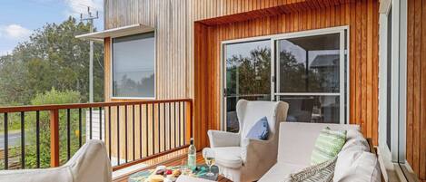 A balcony with a wooden deck, a sofa, two armchairs, and a small table with a cheese board and drinks.