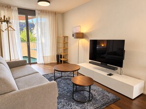 Uma sala de estar moderna com um sofá, duas mesas redondas, uma TV e uma estante.