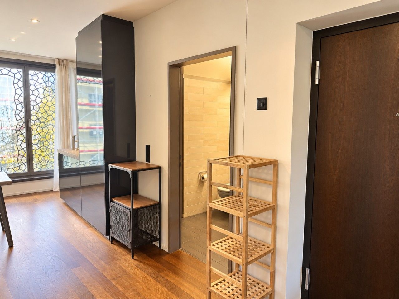 Ein modernes Interieur mit Holzboden, einer schwarzen Regaleinrichtung, einem Holzgestell und einer Tür zu einem Badezimmer.