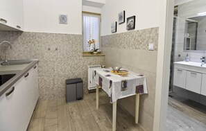 A compact kitchen with a sink, a small table with a tablecloth, and a window with curtains. - Charming Apartment in Murine Near Umag (Umag)