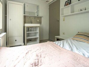 Ein Schlafzimmer mit Bett, Kleiderschrank, Nachttisch, einer Kommode mit einem Bild und einer Tür zu einem anderen Raum.