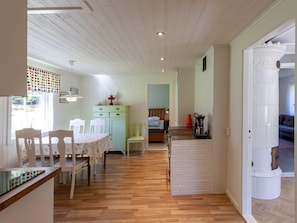 Ein Zimmer mit Holzboden, einem Esstisch mit Stühlen, einem Bett, einer kleinen Küchenzeile und einer Wand aus weißen Ziegeln.