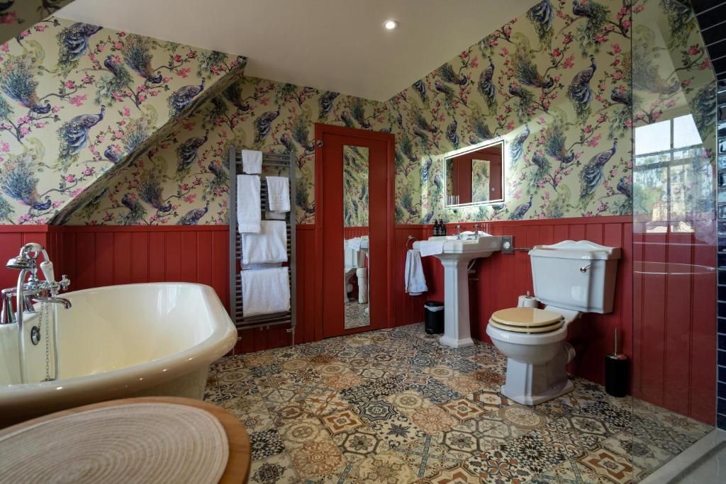 Un baño con una bañera independiente, inodoro, lavamanos y espejo. Las paredes están decoradas con un estampado floral.