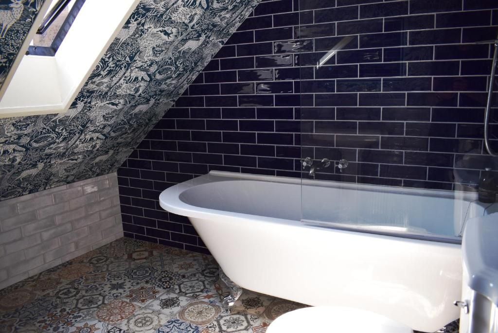 Un baño con bañera independiente, paredes de azulejos y pisos con diseño.