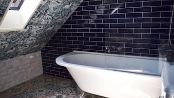 Un baño con bañera independiente, paredes de azulejos y pisos con diseño.