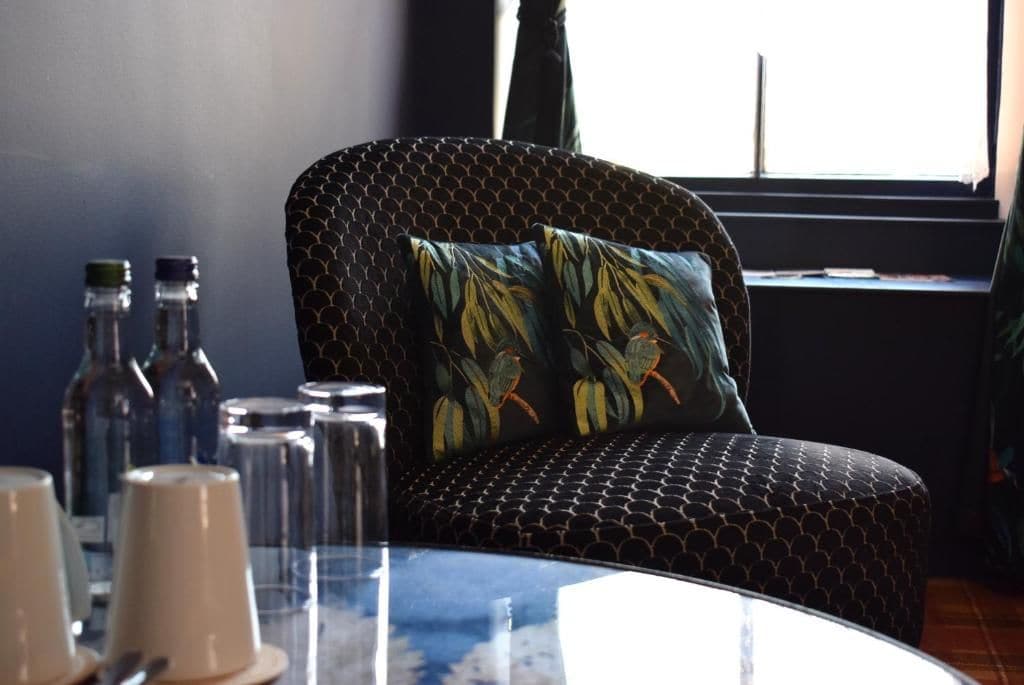 A room with a round table, a patterned armchair, and a window with curtains.