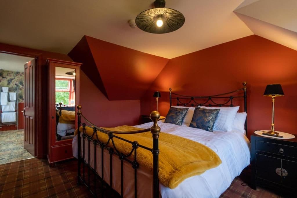 Un dormitorio con cama, mesitas de noche, un espejo y una puerta que da a otra habitación.