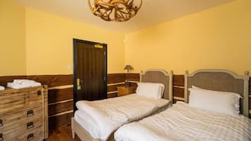 Une chambre d’hôtel avec deux lits, une commode en bois, un lustre et une porte.