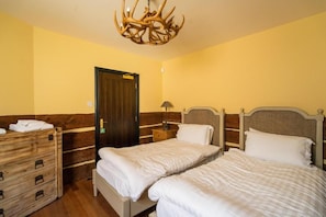 A hotel room with two beds, a wooden dresser, a chandelier, and a door.