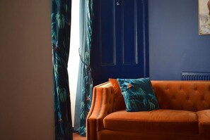 A room with a blue door, an orange sofa with a patterned pillow, and a window with curtains. - The Mash Tun (Charlestown of Aberlour)