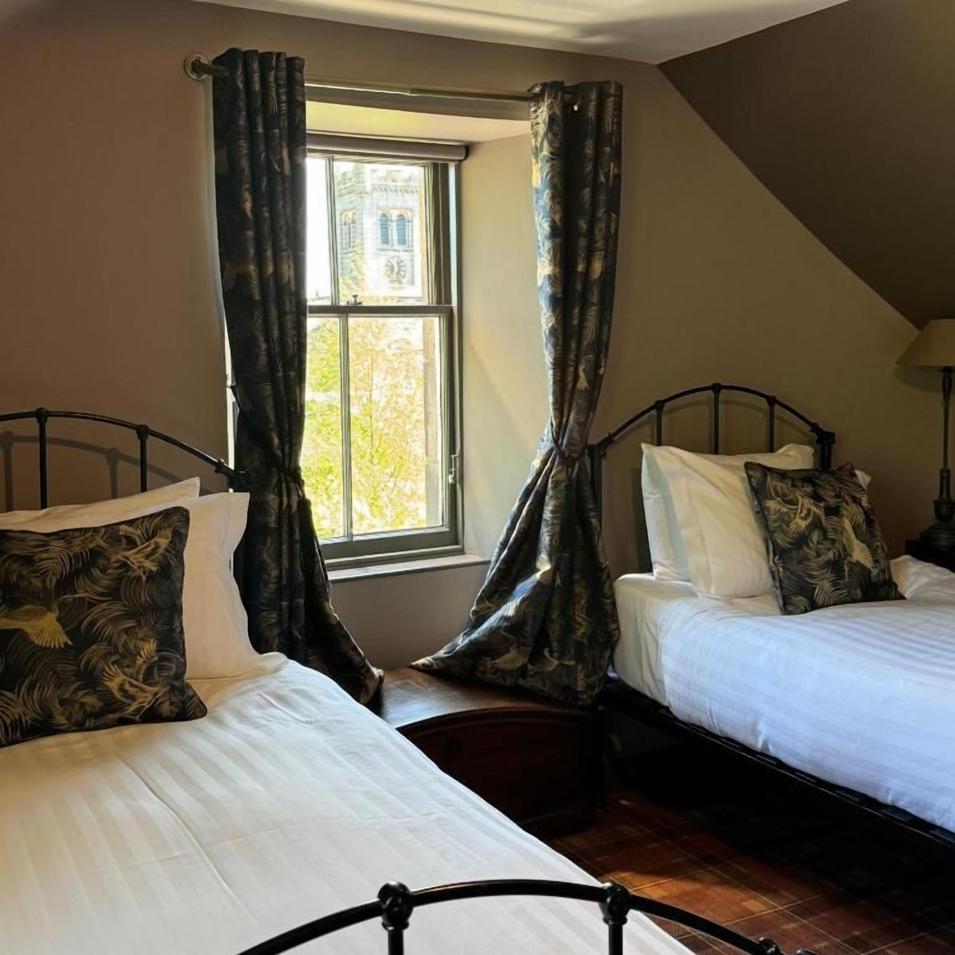 Una habitación con dos camas, una ventana con cortinas y una lámpara.