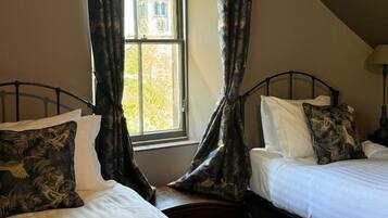 Una habitación con dos camas, una ventana con cortinas y una lámpara.