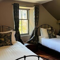 Una habitación con dos camas, una ventana con cortinas y una lámpara.