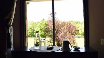 Una mesa con una botella, un vaso y una jarrón junto a una ventana con vistas a árboles.