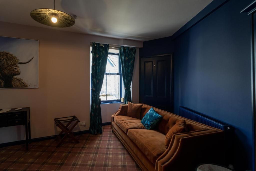 A room with a brown sofa, a small table, a chair, a window with curtains, and a ceiling light fixture.