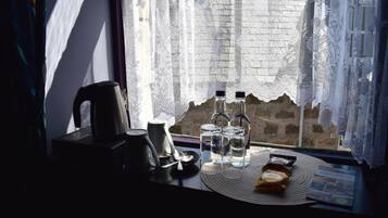 A table with a kettle, cups, and bottles, near a window with lace curtains.