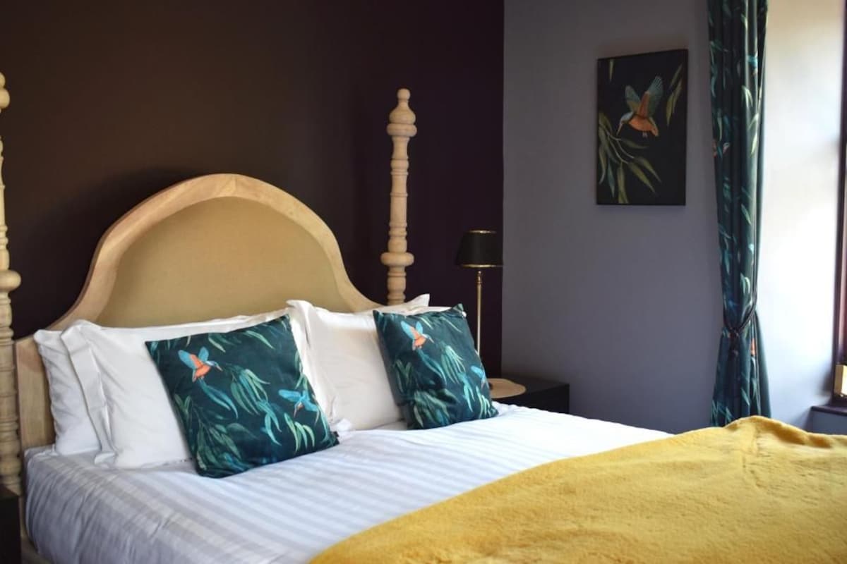 Una cama con cabecera de madera, ropa de cama blanca y una manta amarilla.