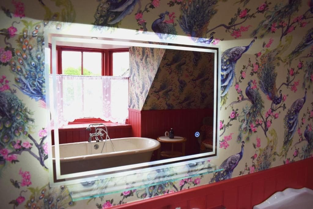Un baño con un espejo grande, papel tapiz con motivos florales y una bañera.