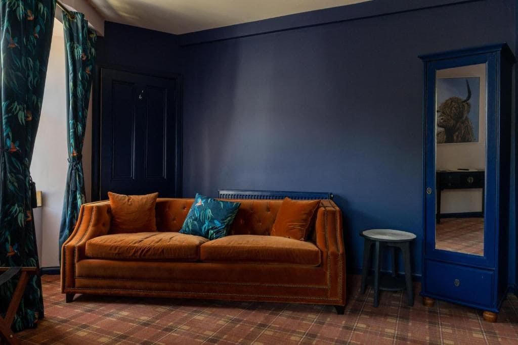 A room with a dark blue wall, a brown sofa with cushions, a small stool, and a blue cabinet with a mirror.