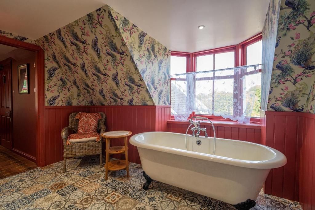Une salle de bain avec une baignoire sur pieds, une chaise en osier, un petit tabouret en bois et un carrelage à motifs.