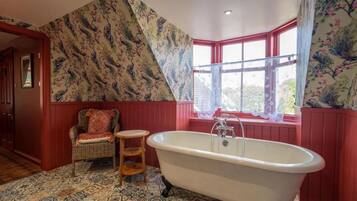 Une salle de bain avec une baignoire sur pieds, une chaise en osier, un petit tabouret en bois et un carrelage à motifs.