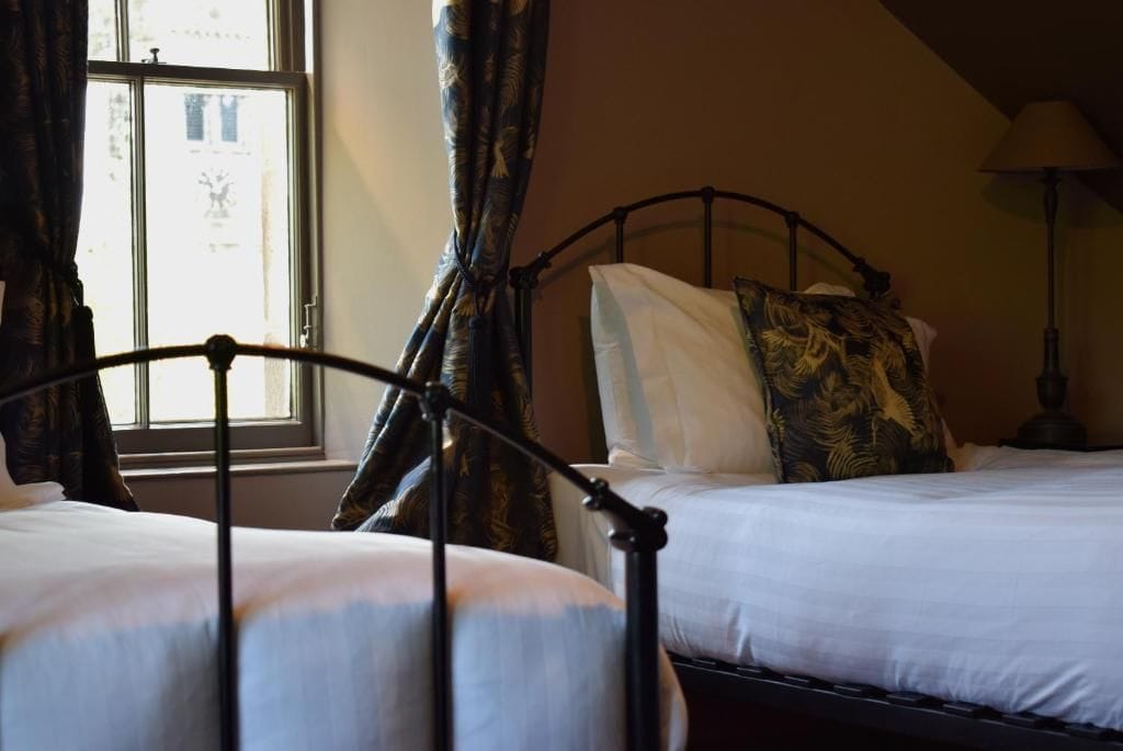 A bedroom with two beds, a window with curtains, and a lamp.