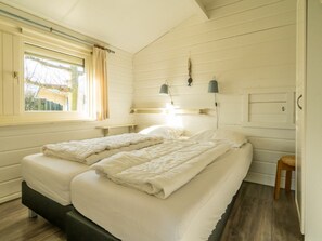 Ein Schlafzimmer mit zwei Betten, einem fensterbelaubten Fenster, Nachttischlampen und einem kleinen Holzschemel.