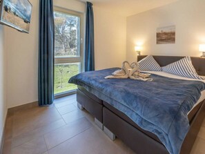 Ein Hotelzimmer mit Bett, einem Fenster mit Vorhängen, einer Wandlampe und einem Gemälde.