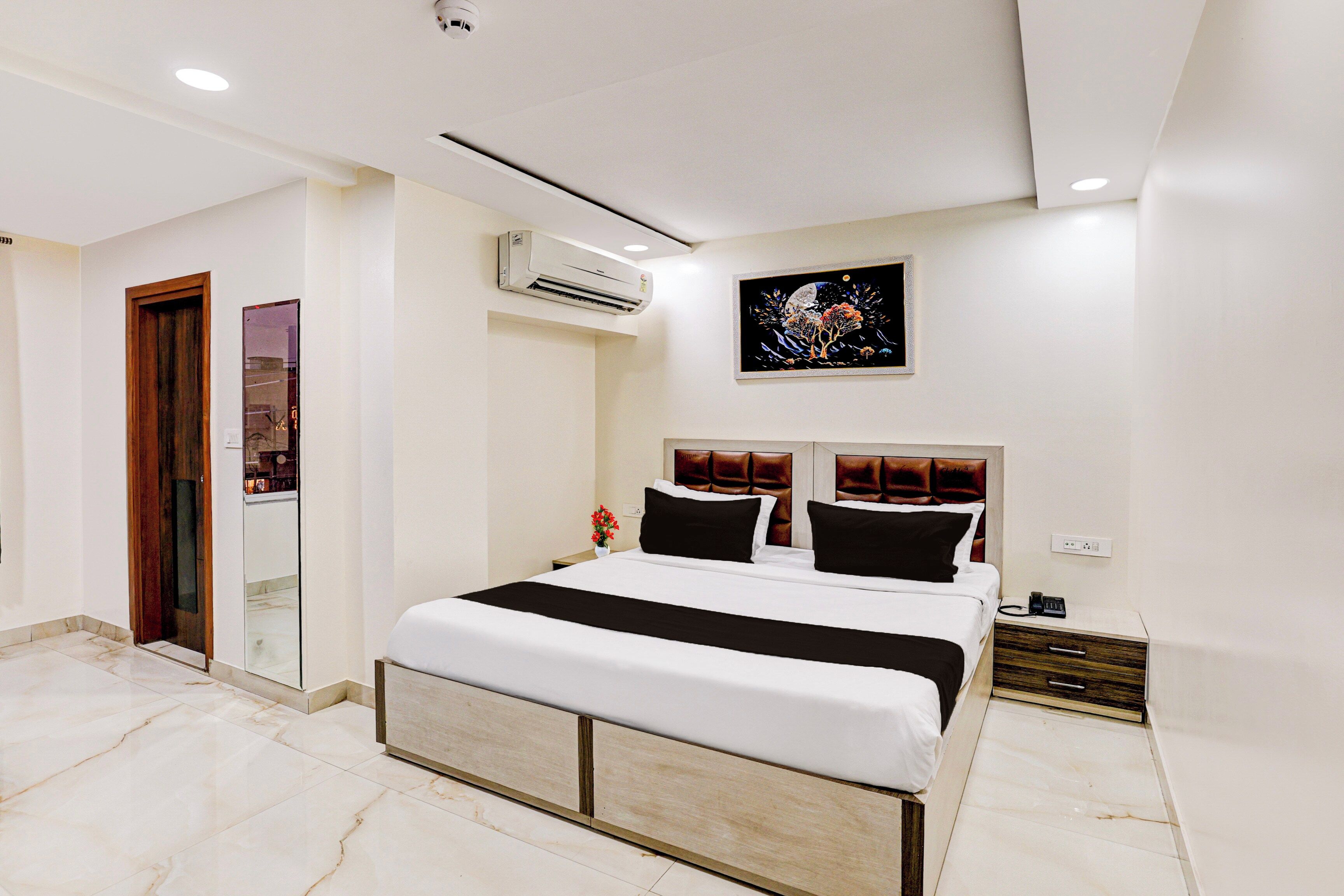 Una habitación de hotel moderna con una cama grande, una mesita de noche, un aire acondicionado instalado en la pared y un cuadro sobre la cama.